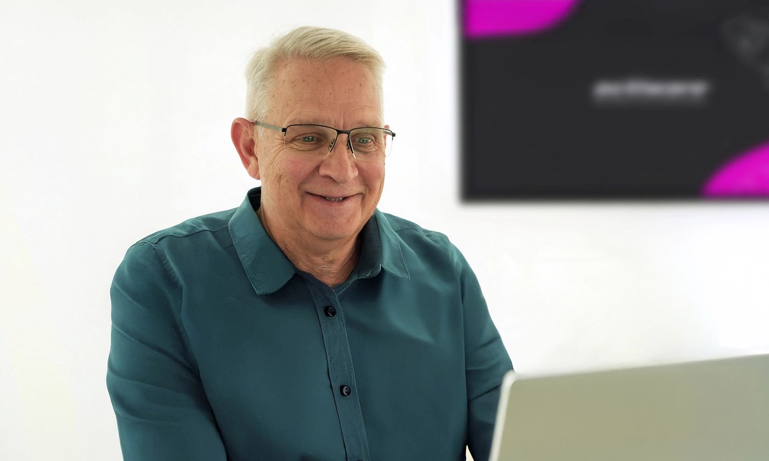 Ein lächelnder Mann mit Brille sitzt vor einem Laptop. Im verschwommenen Hintergrund ist ein Bildschirm mit dem ACTIWARE Design sichtbar.