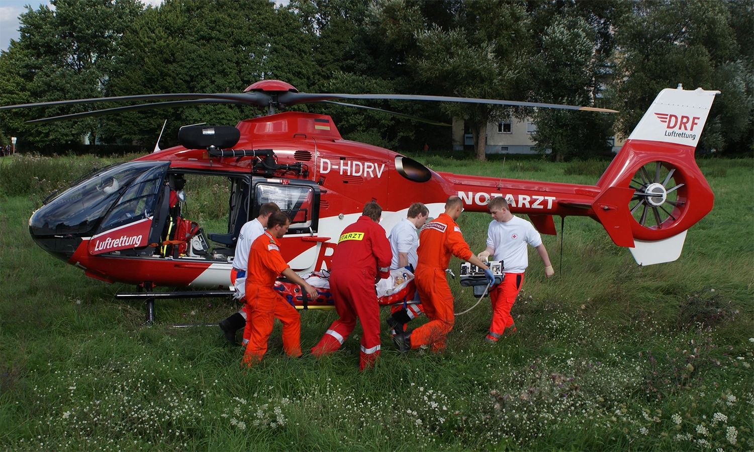 DRF-Luftrettungsteam versorgt einen Patienten neben einem gelandeten Rettungshubschrauber – effiziente Notfallhilfe und medizinische Expertise im Einsatz.