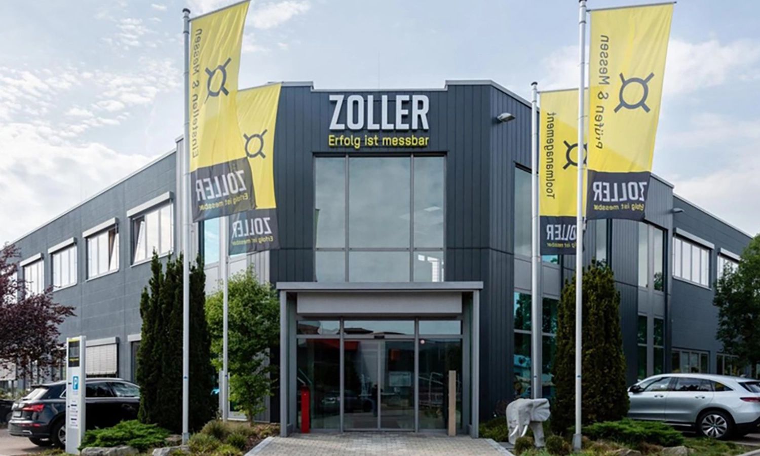 Firmengebäude von e‑zoller mit Fahnen und Eingang – moderner Unternehmenssitz für Präzisionsmesstechnik und digitale Werkzeugverwaltung.