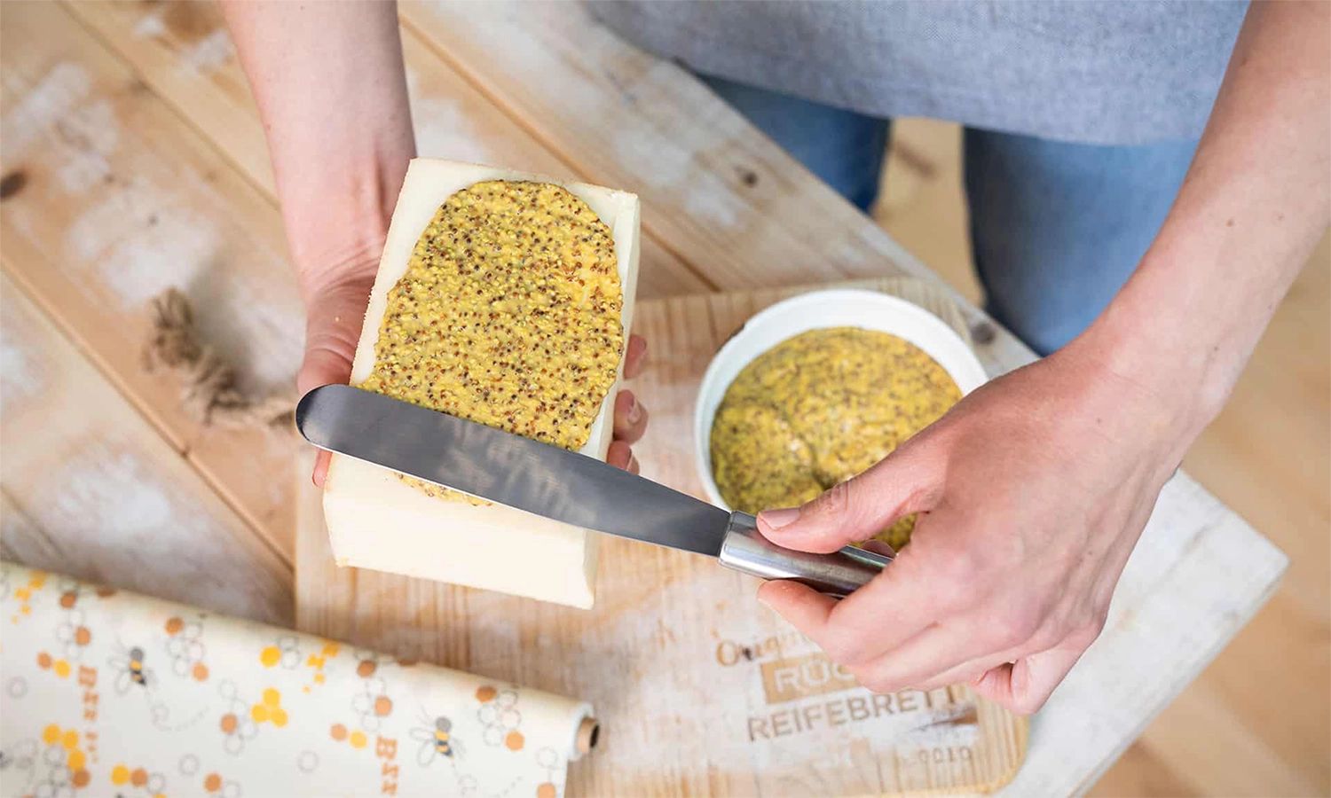Person streicht Senfbutter auf ein Stück Rücker‑Käse – handwerkliche Zubereitung und Genussmoment mit norddeutscher Käsespezialität.