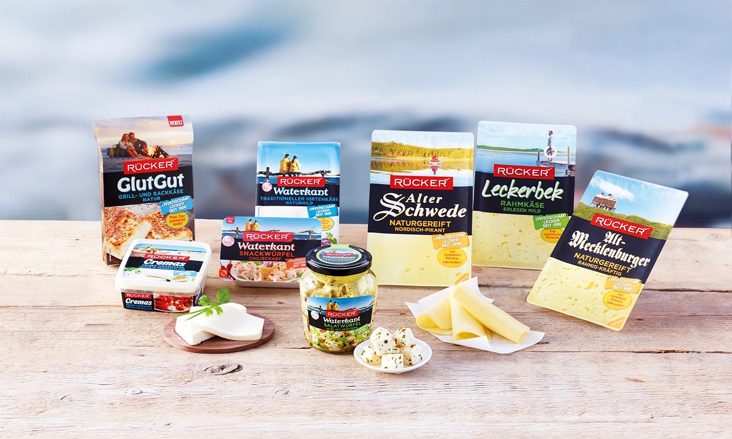 Verschiedene Rücker‑Käseprodukte auf Holztisch – Sortiment norddeutscher Spezialitäten wie Alter Schwede, Waterkant und Alt‑Mecklenburger aus der Familienmolkerei Rücker.