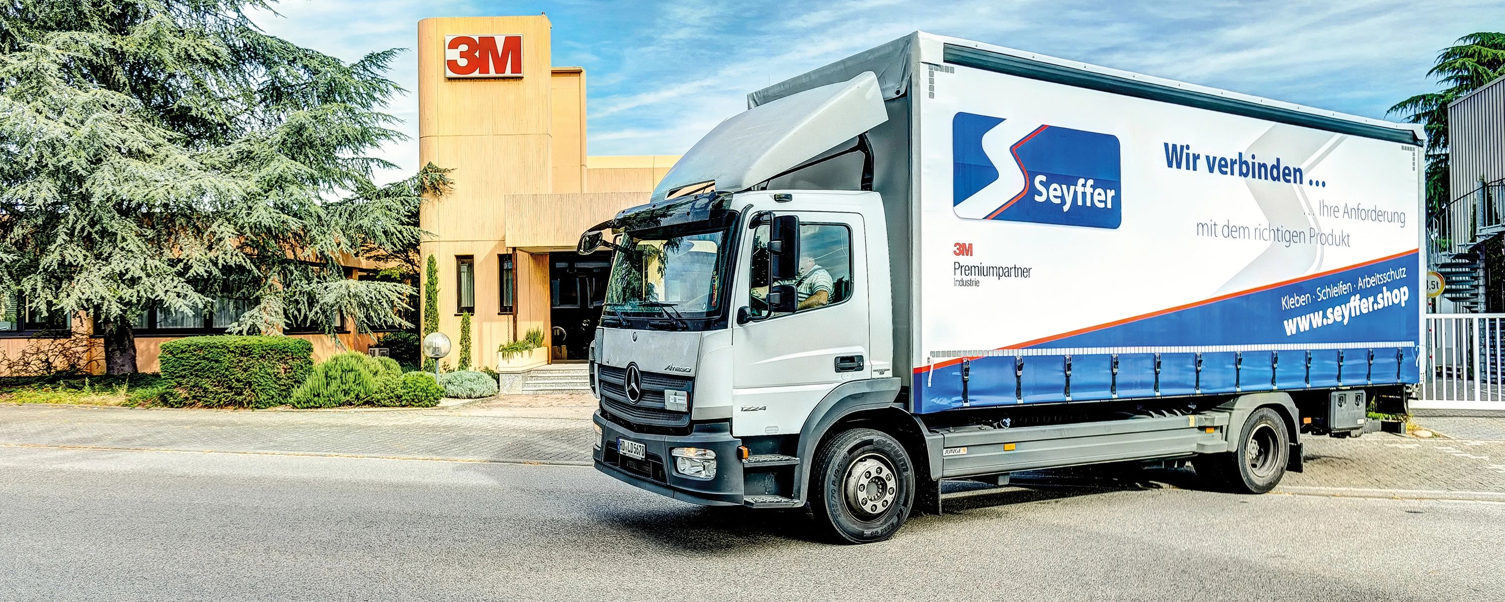 Seyffer‑LKW vor einem Firmengebäude – Transportfahrzeug mit Firmenlogo und Slogan ‚Wir verbinden …‘, Partnerunternehmen im Bereich Klebe‑ und Verbindungstechnik.