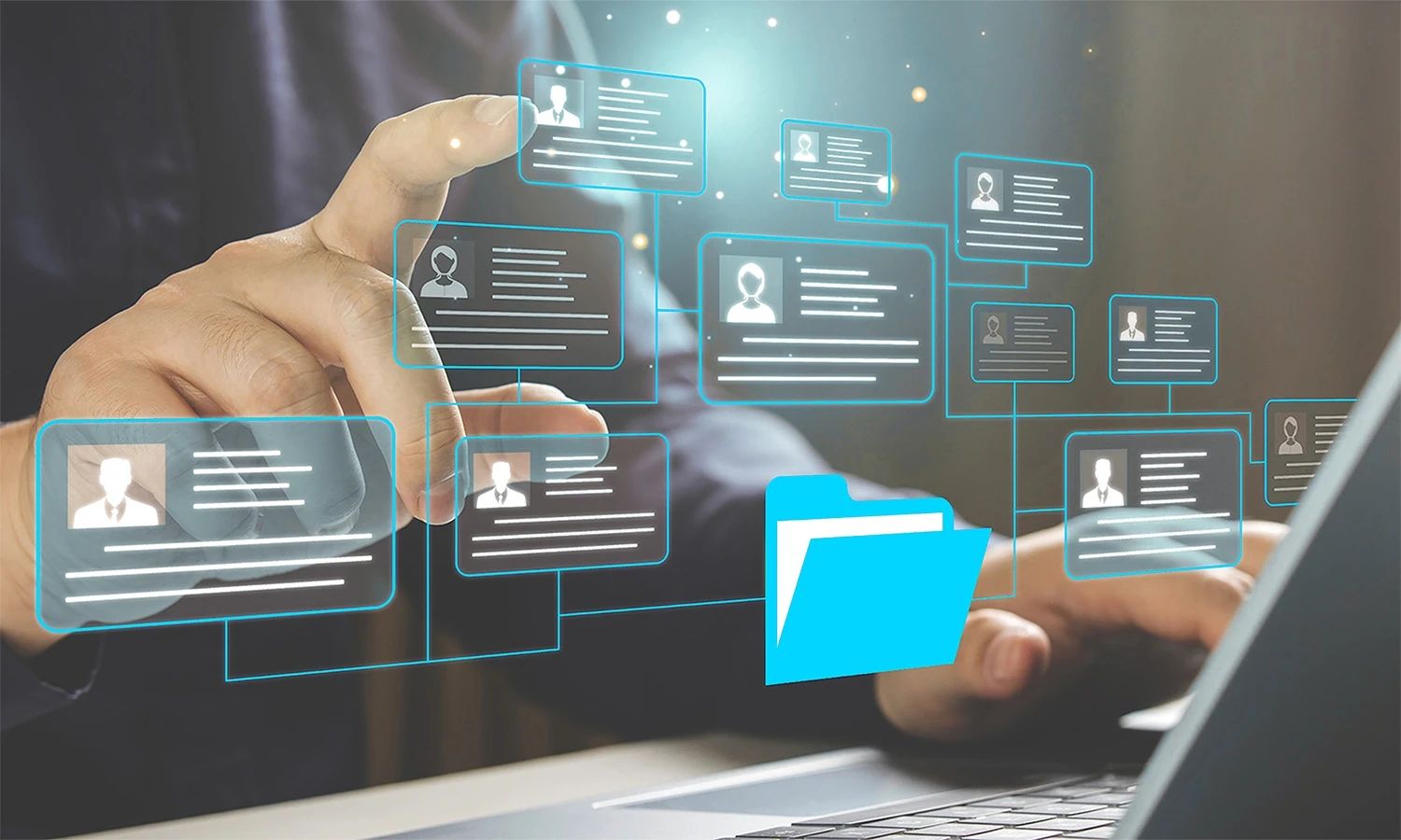 Nahaufnahme der Hände einer Person, die über einer Laptoptastatur arbeitet und mit dem Finger digitale, leuchtend blaue Icons von Personalakten und Profilen berührt. Diese Akten-Icons sind untereinander vernetzt und führen zu einem zentralen, leuchtend blauen Ordnersymbol, was die digitale Verwaltung von Mitarbeiterdaten darstellt.