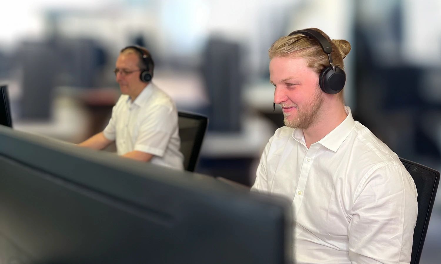 Zwei Support-Mitarbeiter mit Headsets arbeiten im Büro an ihren Computern.