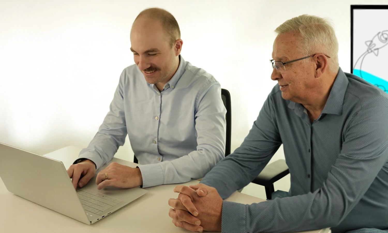 Zwei Männer sitzen gemeinsam an einem Schreibtisch und schauen auf einen Laptop. Beide lächeln und wirken konzentriert. Im Hintergrund ist ein Bildschirm mit dem Logo „actiware“ zu sehen.