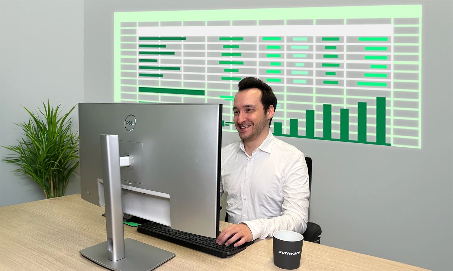 Lächelnder Mitarbeiter vor einem Monitor, hinter dem eine große, leuchtende Projektion von Invoice-Tabellen und grünen Balkendiagrammen (Datenanalyse) zu sehen ist.