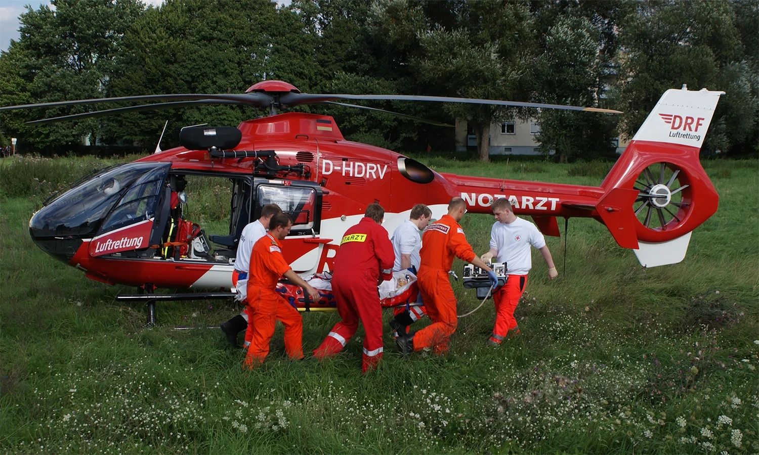 DRF-Luftrettungsteam versorgt einen Patienten neben einem gelandeten Rettungshubschrauber – effiziente Notfallhilfe und medizinische Expertise im Einsatz.