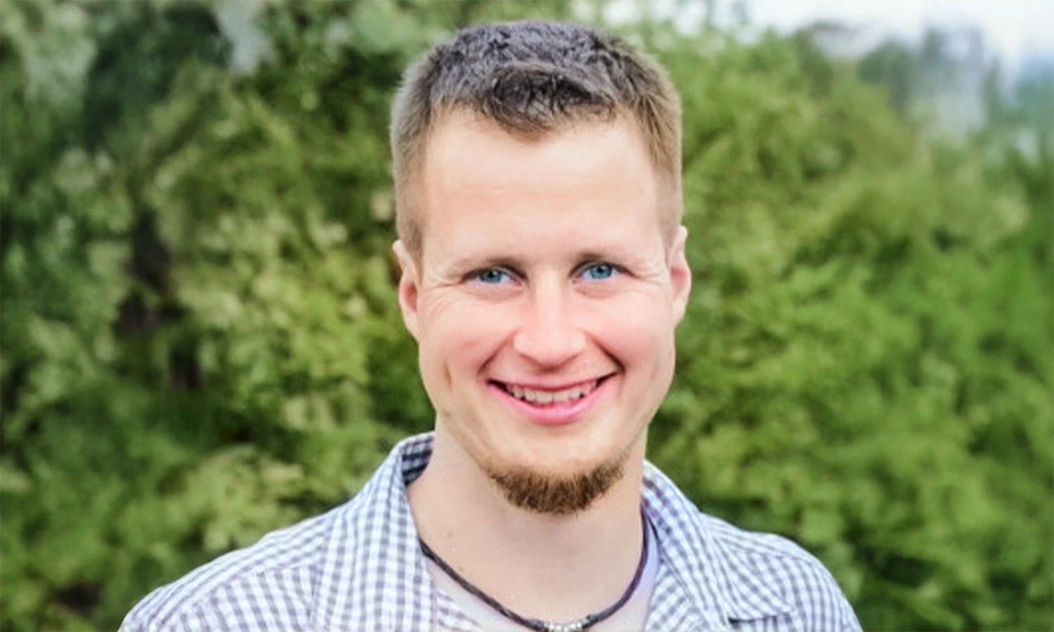 Porträtfoto eines lächelnden Mannes im Freien vor grünem Hintergrund – Mitarbeiterfoto der HF Mixing Group für Unternehmenskommunikation.