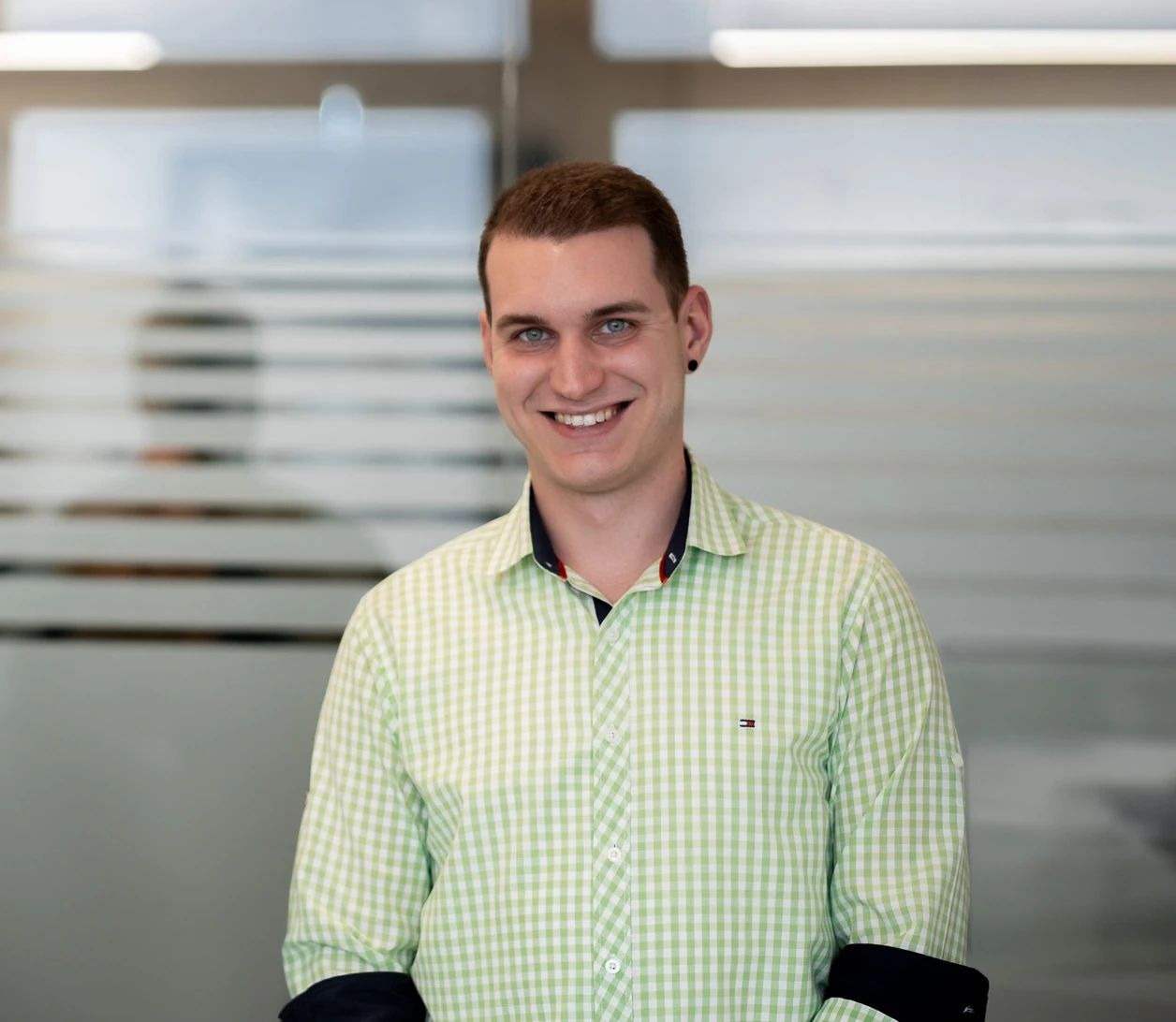 Rosenberg‑Mitarbeiter im grünen karierten Hemd vor Glaswand – Porträtfoto eines Teammitglieds des Lüftungs‑ und Klimatechnikunternehmens, das Kompetenz und Offenheit ausstrahlt.