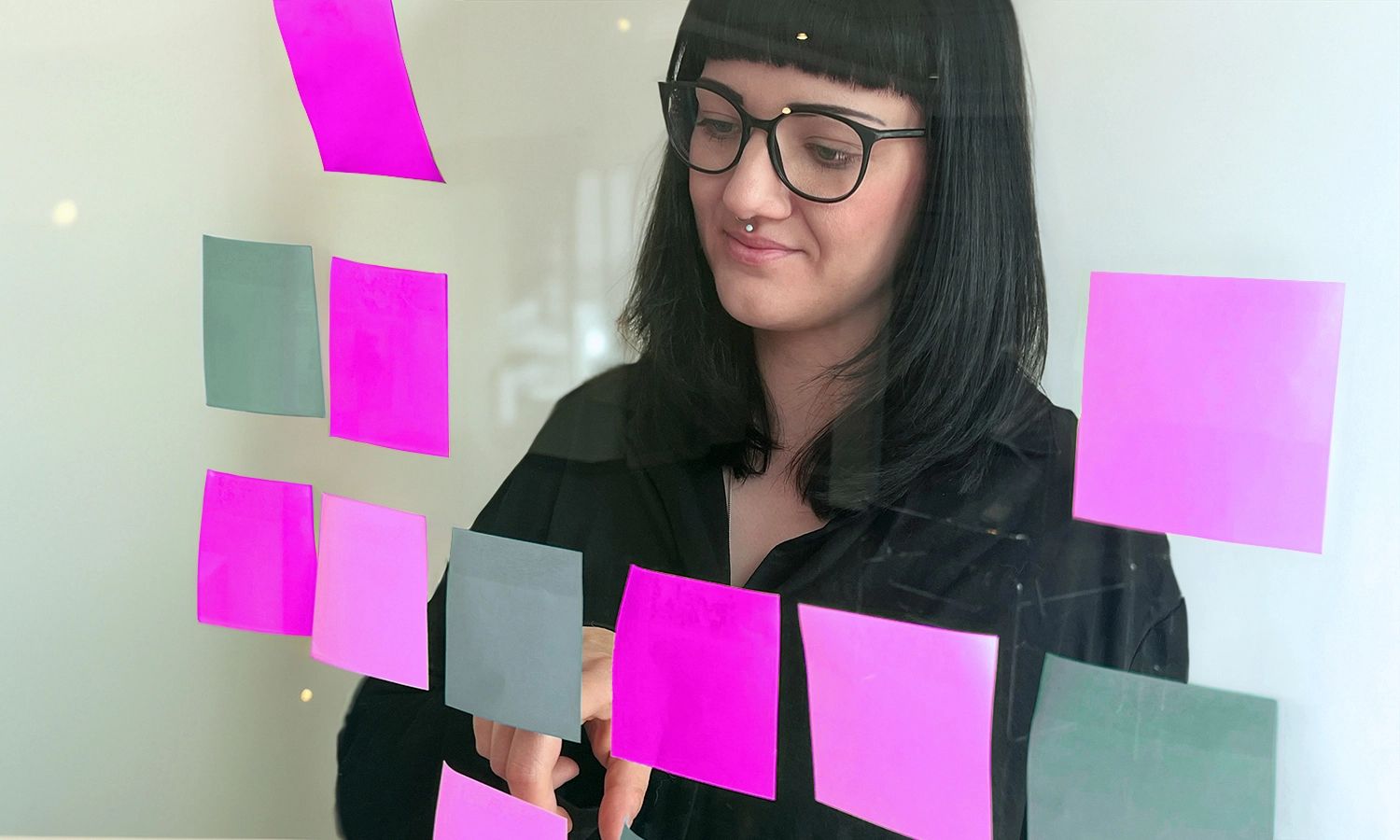 Eine Mitarbeiterin steht vor einer Glaswand, an der bunte Zettel haften, und beteiligt sich aktiv an einem Workshop