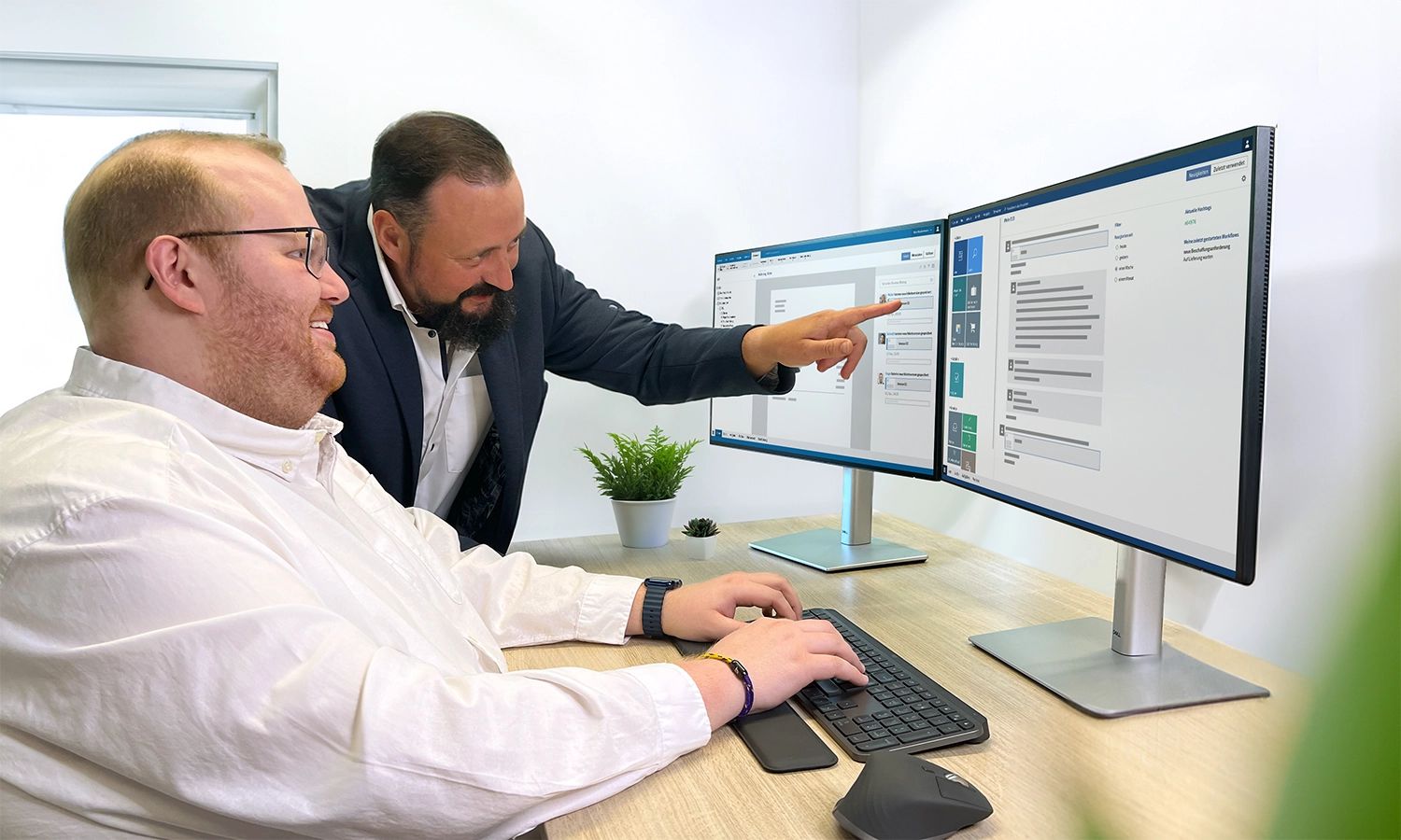 Ein erfahrener Mitarbeiter erklärt einem Kollegen die Funktionen der ELO ECM Suite und zeigt ihm die Benutzeroberfläche auf einem Dual-Monitor-Setup.
