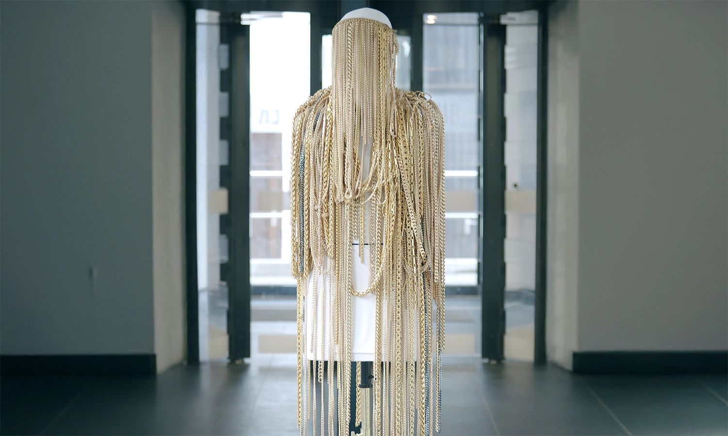 Kunstvolle Installation aus goldfarbenen Metallketten auf einer weißen Figur – Kombination aus Design, Handwerk und Innovation.