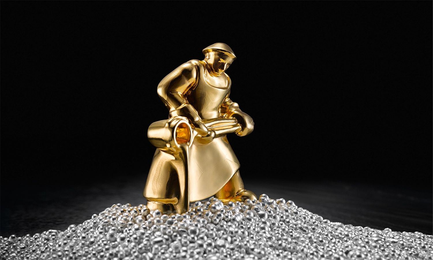 Goldene Figur eines Gießers auf einem Haufen aus Silbergranulat – Symbol der Heimerle + Meule GmbH für Edelmetallverarbeitung, Präzision und traditionelle Handwerkskunst.
