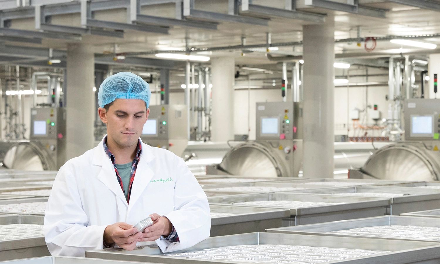 Mitarbeiter in Landguth‑Produktionshalle prüft Tiernahrungsdosen – Qualitätskontrolle und Lebensmittelsicherheit in moderner Fertigung.