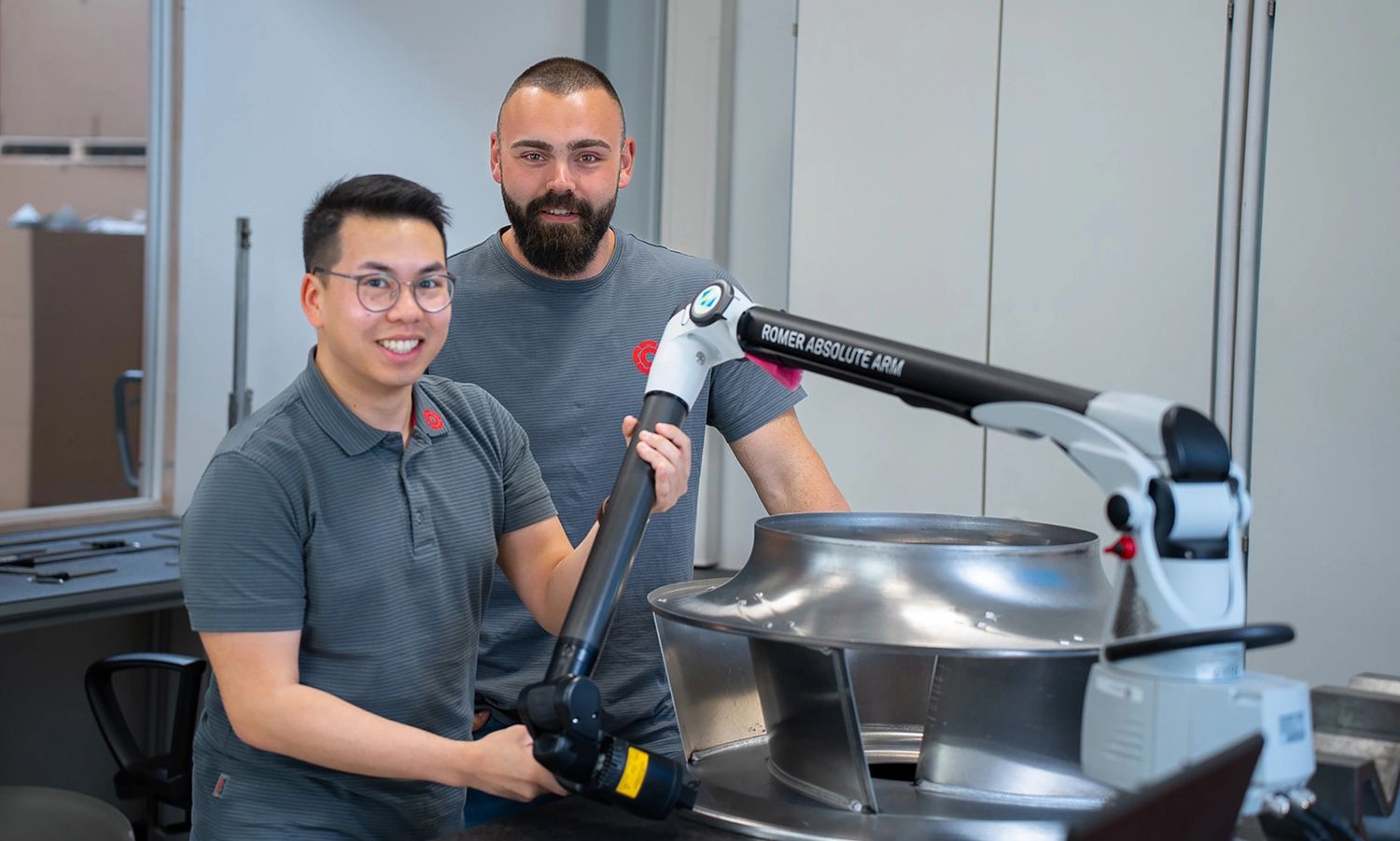 Zwei Rosenberg‑Mitarbeiter bei der Arbeit mit einem 3D‑Messarm neben einem Industrieventilator – Präzisionsmessung und Qualitätskontrolle in der Fertigung.