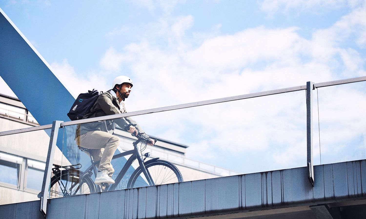 Städtischer Radfahrer mit Helm und Rucksack fährt über Brücke – modernes Urban‑Commuting mit Schwalbe‑Reifen für Alltag und Pendelverkehr.