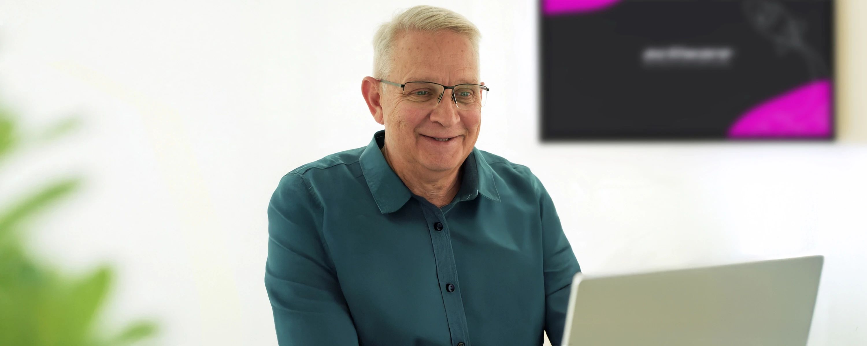 Ein lächelnder Mann mit Brille sitzt vor einem Laptop. Im verschwommenen Hintergrund ist ein Bildschirm mit dem ACTIWARE Design sichtbar.