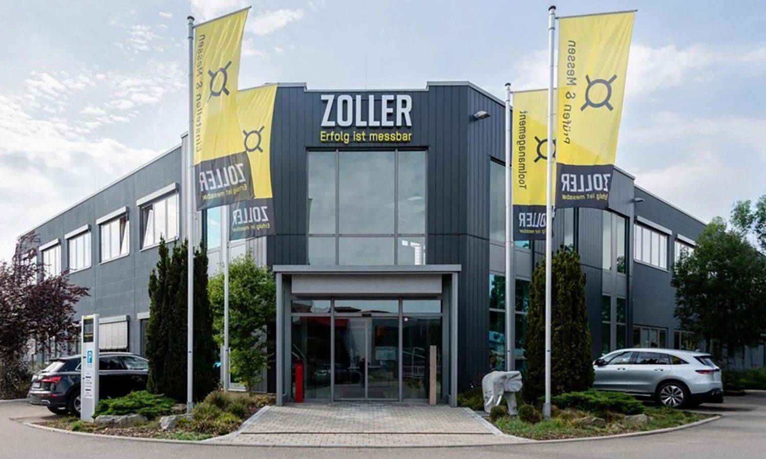 Firmengebäude von e‑zoller mit Fahnen und Eingang – moderner Unternehmenssitz für Präzisionsmesstechnik und digitale Werkzeugverwaltung.