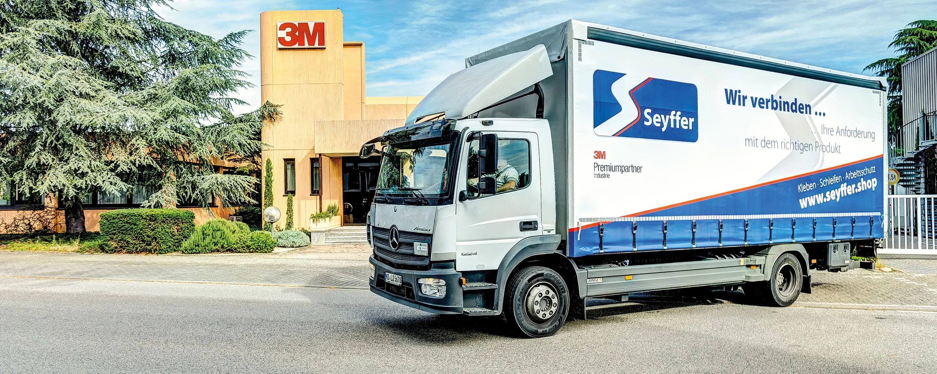 Seyffer‑LKW vor einem Firmengebäude – Transportfahrzeug mit Firmenlogo und Slogan ‚Wir verbinden …‘, Partnerunternehmen im Bereich Klebe‑ und Verbindungstechnik.